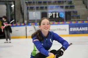 Smiling young curler on the ice holding a curling stick